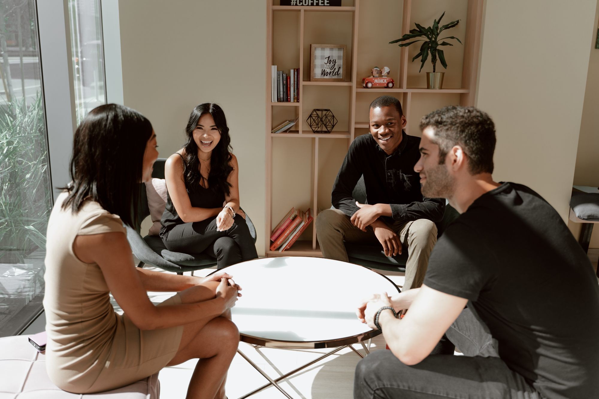 Quatro pessoas conversando ao redor de uma mesa em um ambiente iluminado. Fotografia ilustrativa.