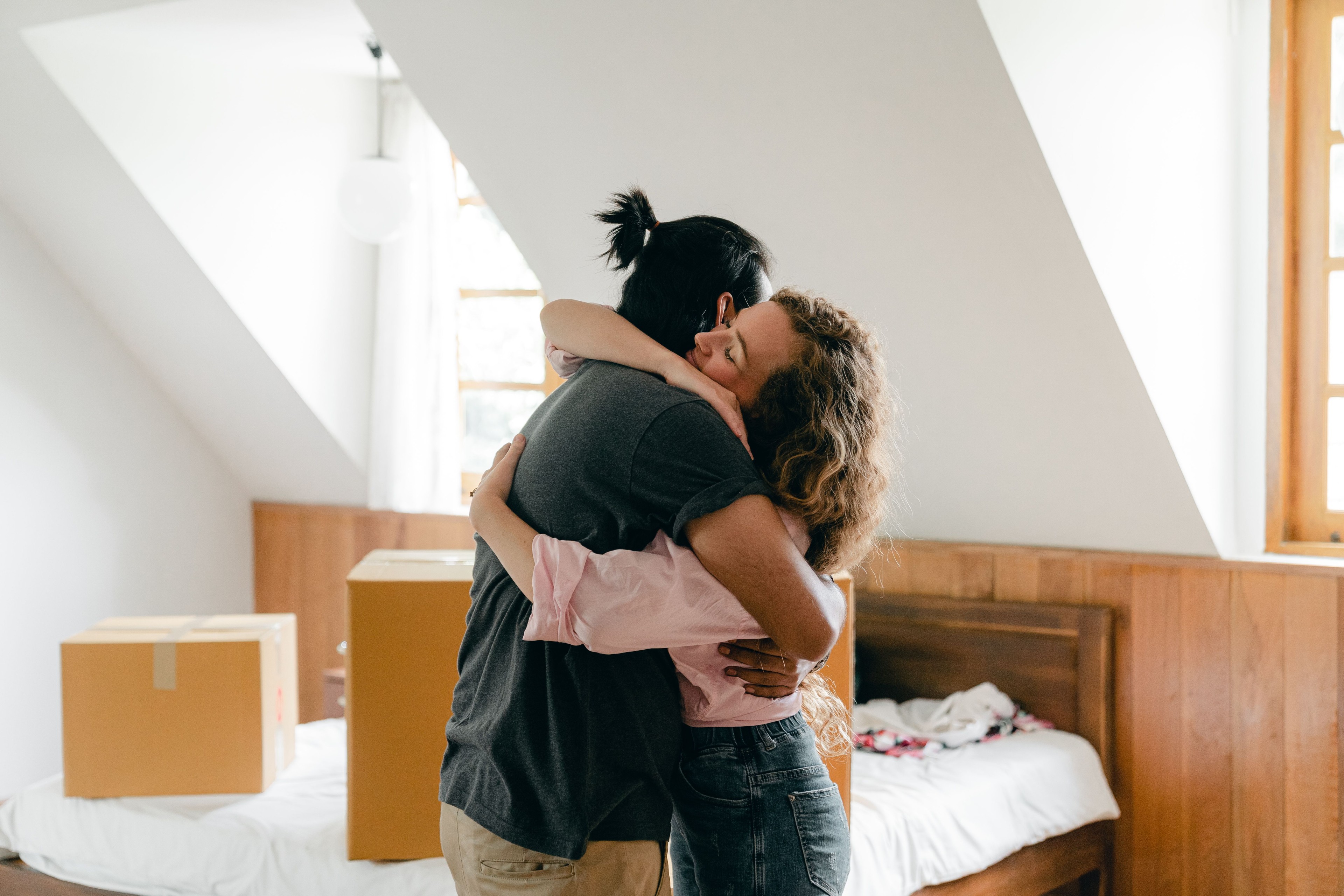 Casal se abraça em um quarto iluminado, entre caixas de mudança